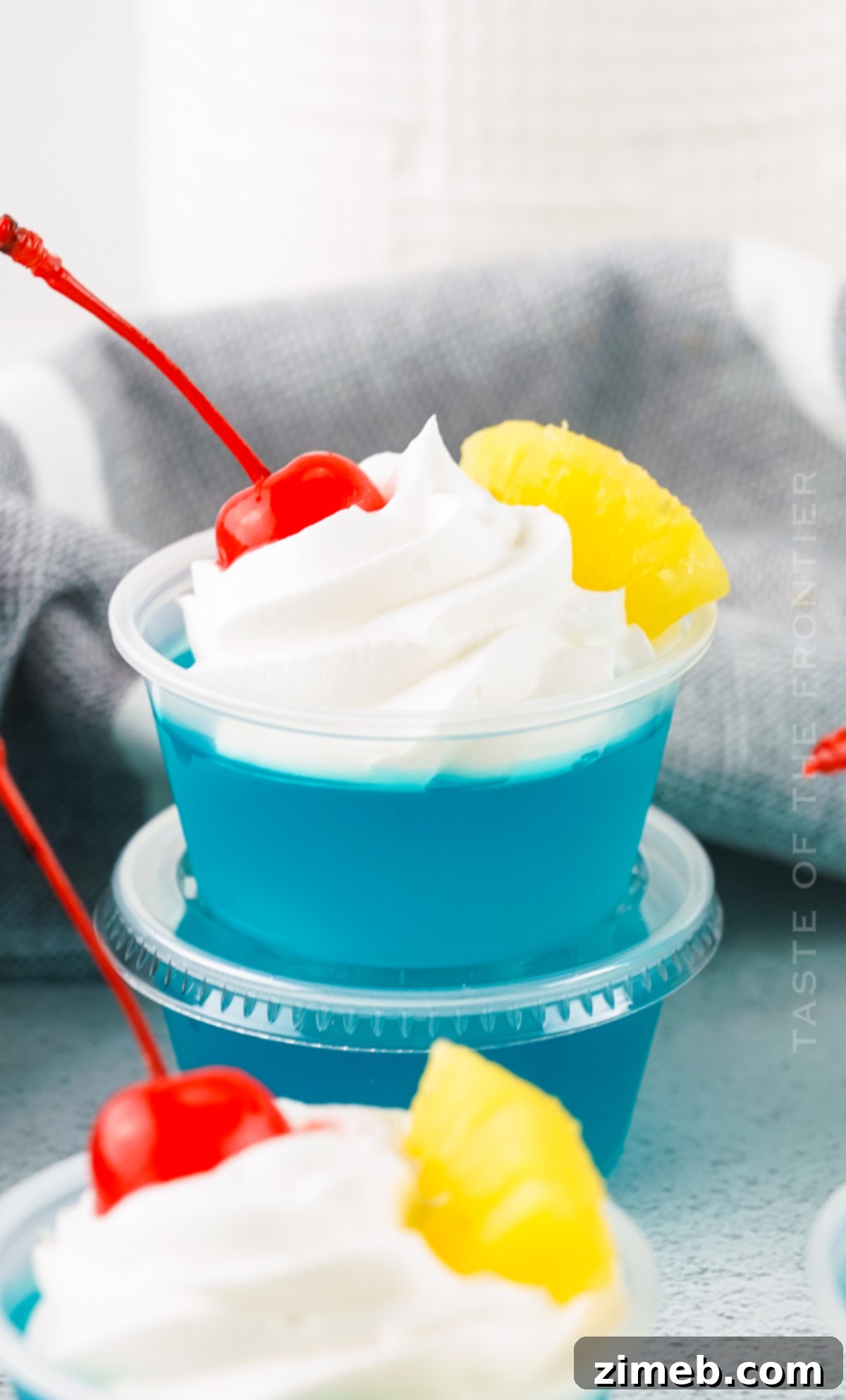 A tray of small plastic cups filled with bright blue Jello Shots, garnished with tiny umbrellas, ready for a beach-themed party.