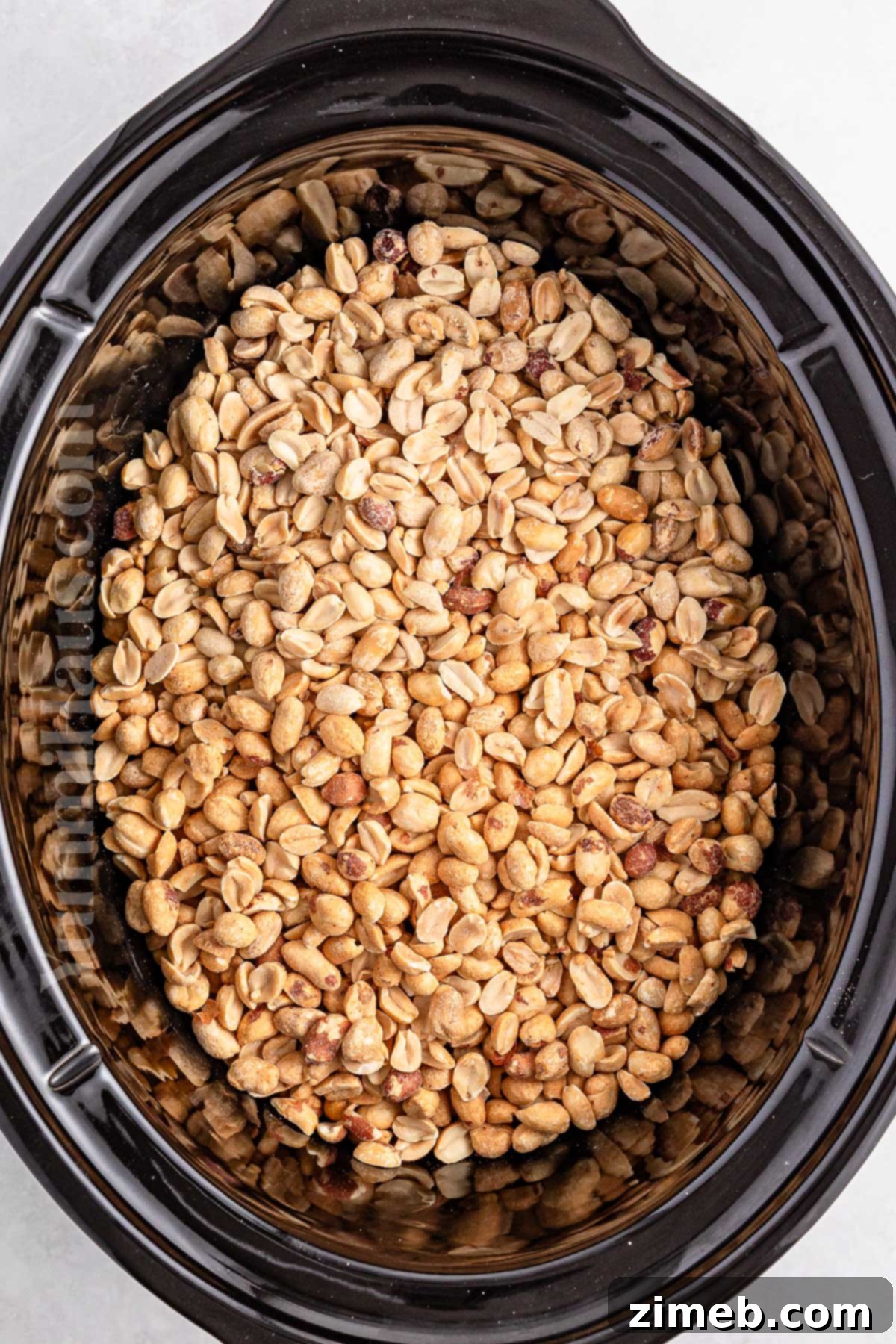 Layering peanuts, chocolate, and peanut butter chips in a slow cooker insert for candy making.