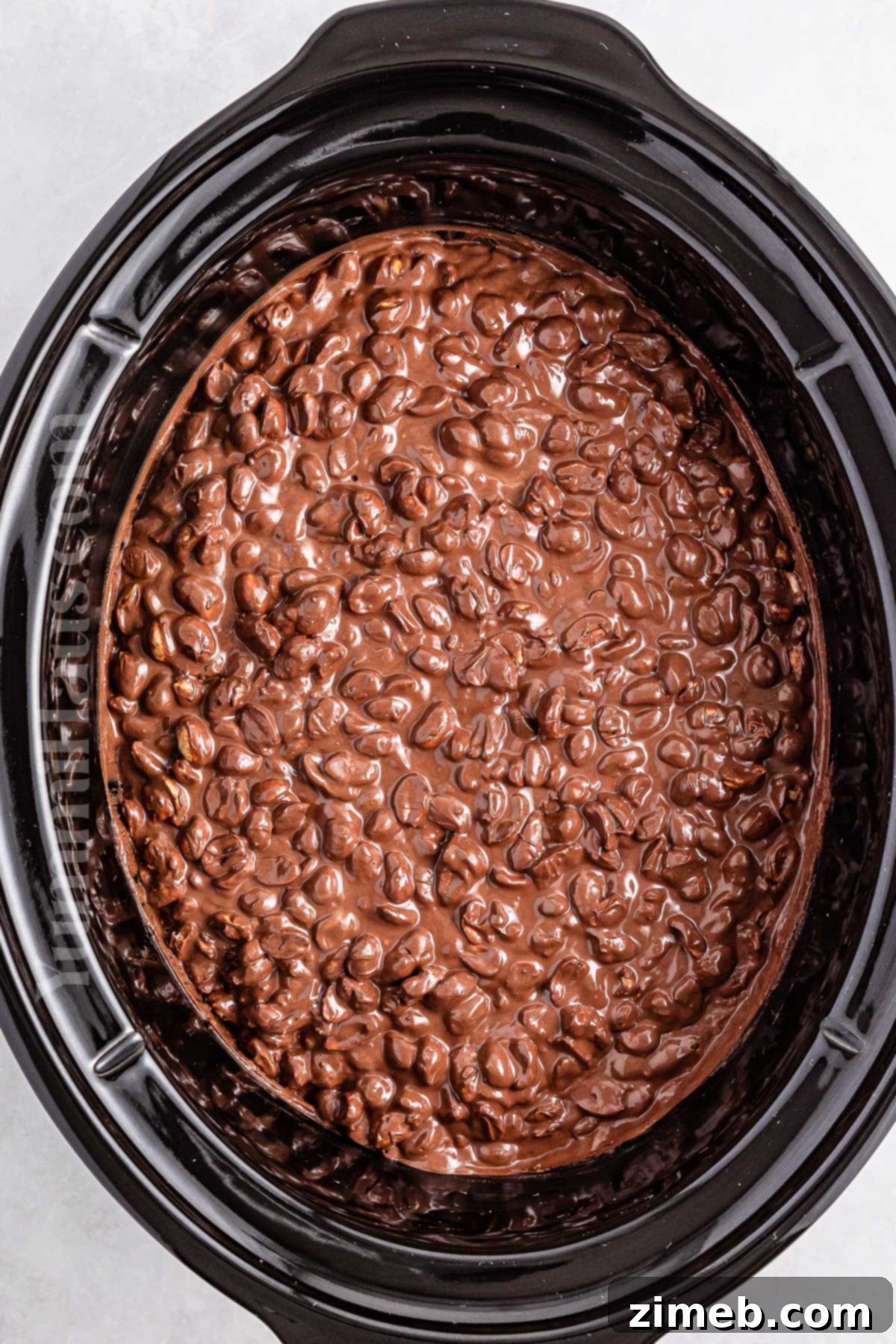 Melted chocolate and peanuts mixed together in a slow cooker, ready for portioning.