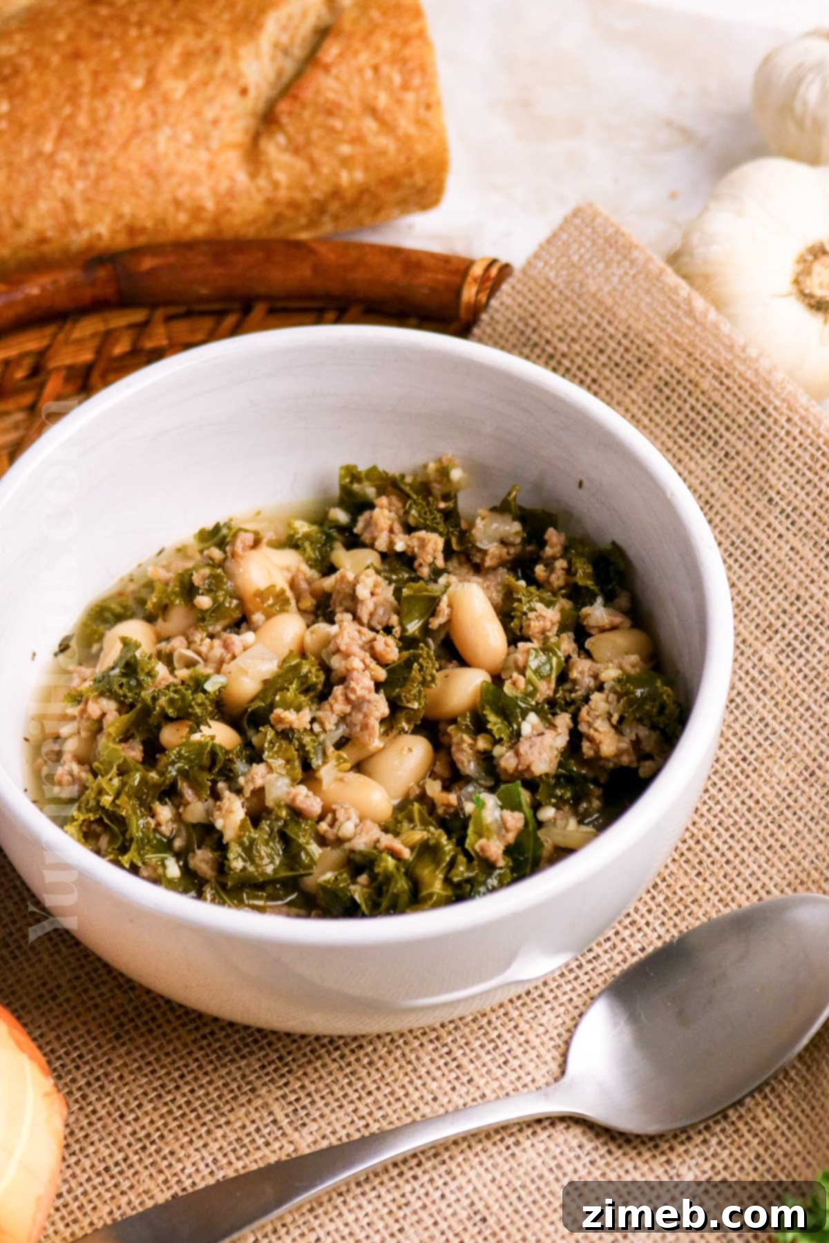 Tuscan Sausage, Kale, and White Bean Soup 14 A rustic presentation of a bowl of Cannellini Bean, Sausage, and Kale Soup with a spoon, ready to be eaten.