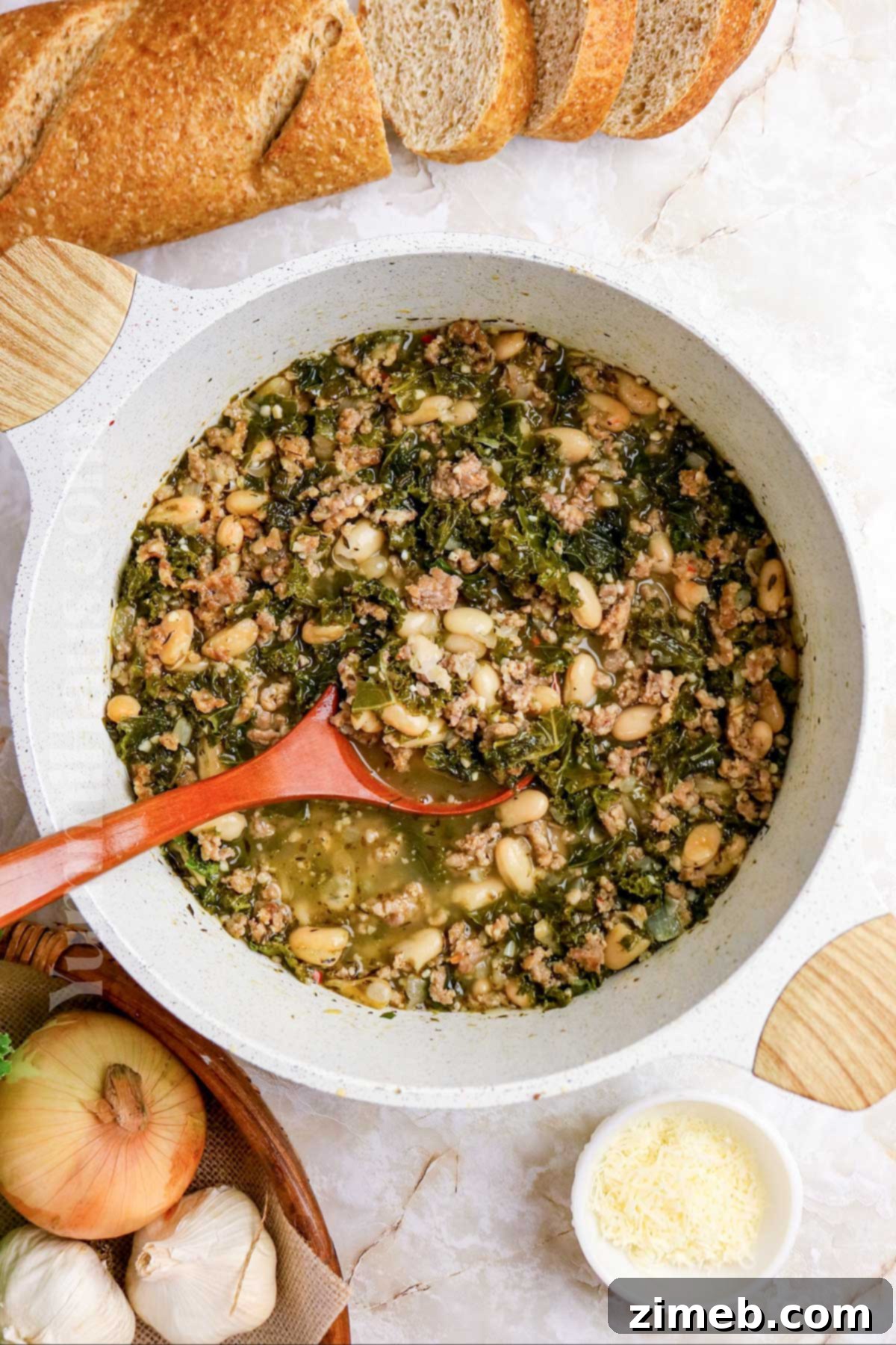 Tuscan Sausage, Kale, and White Bean Soup 3 A serving of Cannellini Bean, Sausage, and Kale Soup with crusty bread on a rustic wooden table.