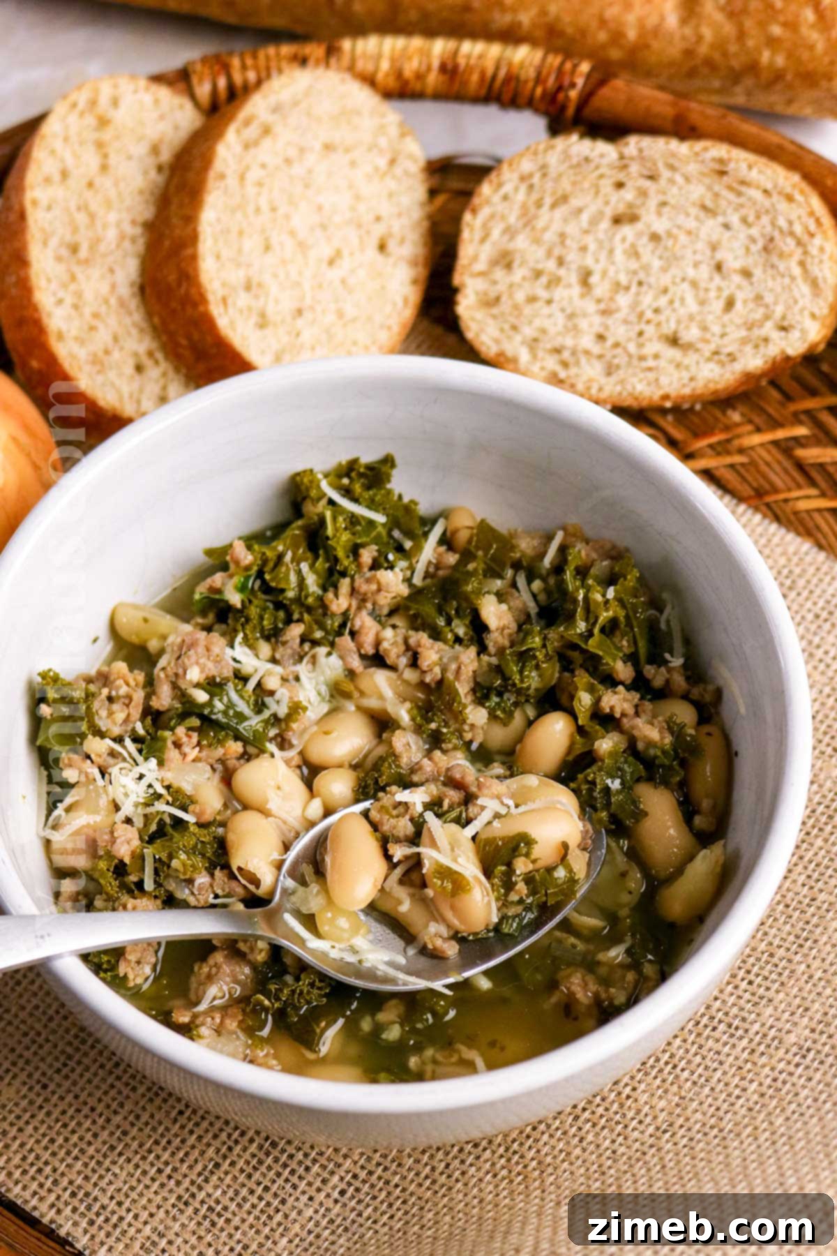 Tuscan Sausage, Kale, and White Bean Soup 8 A steaming bowl of Cannellini Bean, Sausage, and Kale Soup on a rustic wooden surface, ready for a cozy meal.