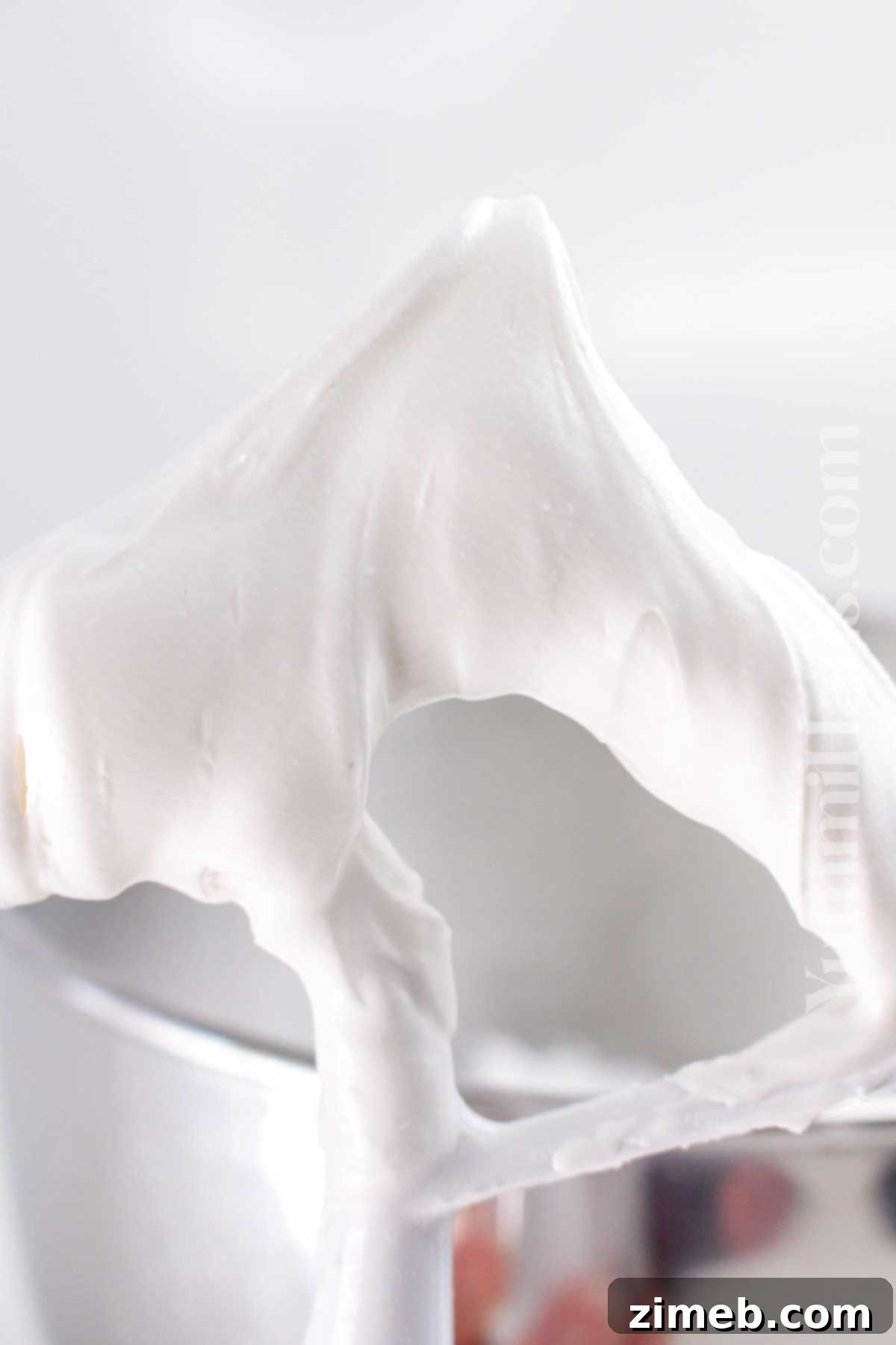 Royal icing being beaten in a stand mixer, demonstrating the process to achieve stiff peaks.