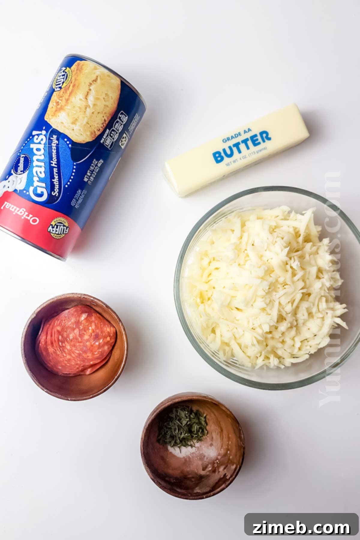 Ingredients for Pizza Muffins laid out on a cutting board, including biscuit dough, pepperoni, cheese, and butter.