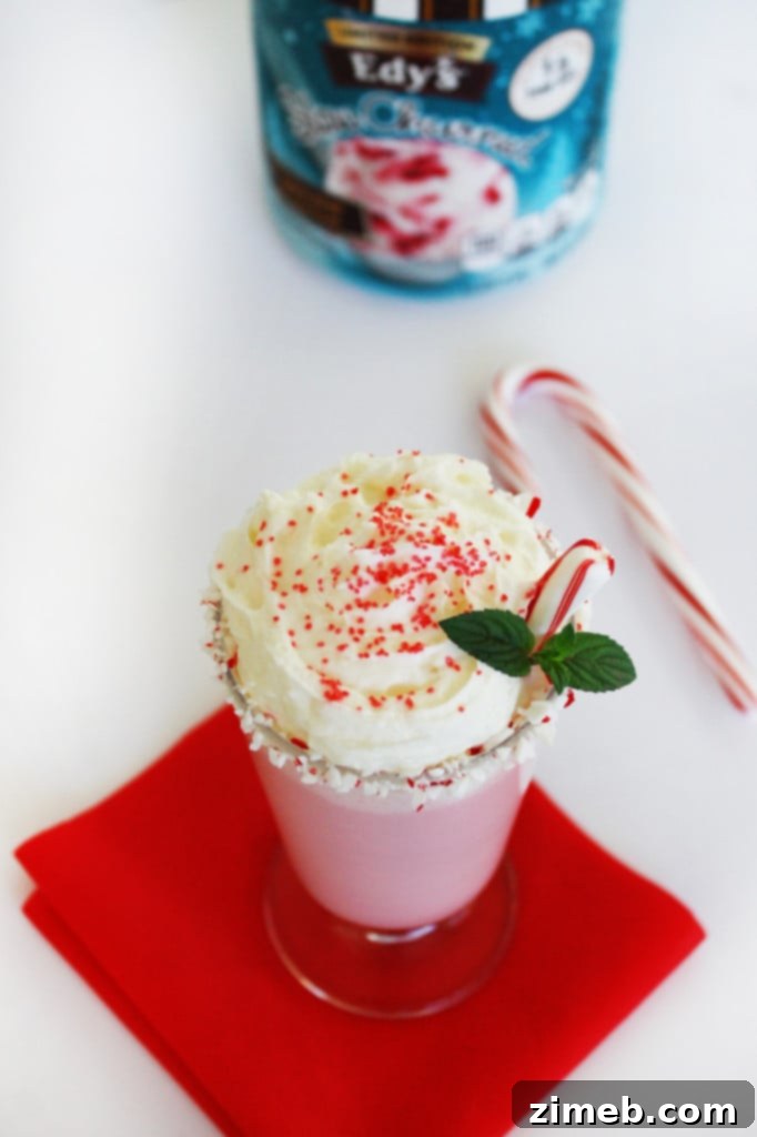 A vibrant green peppermint milkshake, generously topped with fluffy whipped cream, festive sprinkles, and a candy cane, an irresistible treat for holiday celebrations.