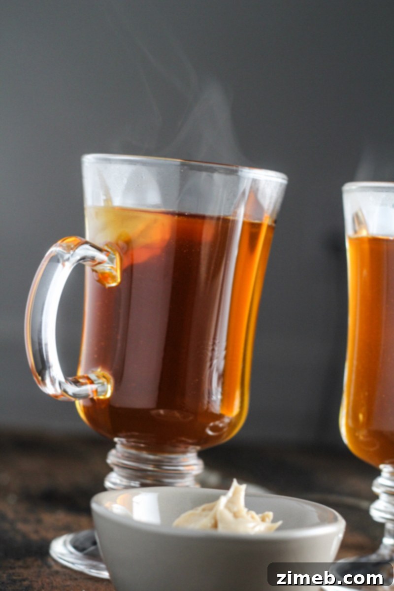 A rich, steaming mug of Burnt Sugar Hot Buttered Rum, topped with a dollop of whipped cream and a sprinkle of cinnamon, a decadent and warming holiday indulgence.