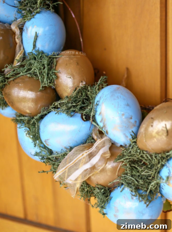 Elegant Blue and Gold Easter Wreath 3 Close-up of a DIY spring wreath adorned with robin's egg blue and gold painted faux eggs, nestled among green moss on a grapevine base.