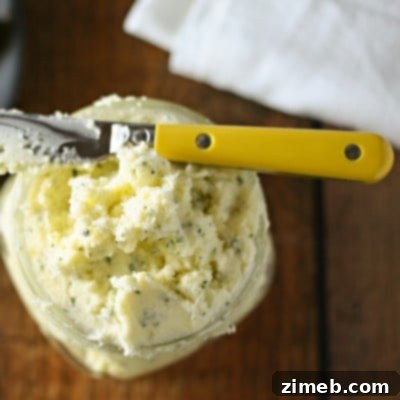 Overhead view of whipped butter with garlic and chives in a jar with a butter knife laying on top.