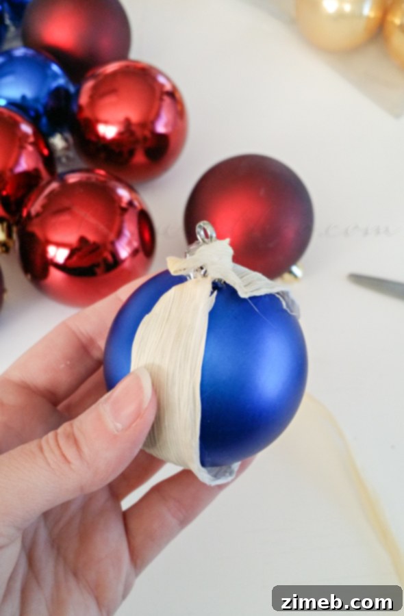 Wildcrafted Wonders 4 Close-up of a hand carefully wrapping a traditional spherical Christmas ornament with strips of natural materials like corn husks, ripped muslin, and rough burlap