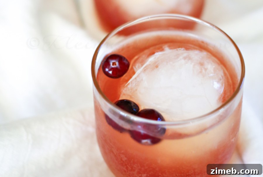 Crimson Ember 3 Two glasses of Cranberry Whiskey Cocktail on a festive background, with a decorative bowl of cranberries.