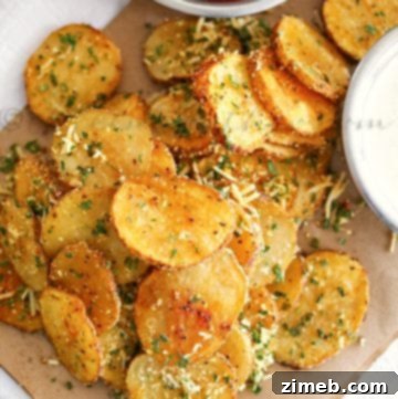 Crispy Parmesan Potatoes 11 Overhead view of roasted potato slices topped with grated parmesan cheese on a parchment covered plate with two dipping sauces.
