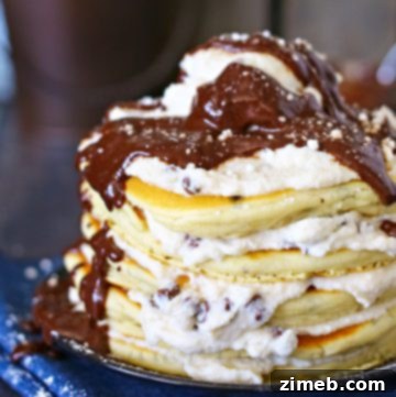 A stack of Cannoli Pancakes with a large scoop of filling on top, dusted with confectioners sugar and drizzled with chocolate syrup