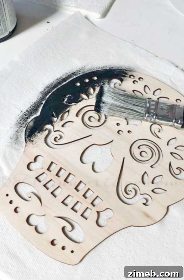Black paint being applied to a sugar skull cutout for a Halloween wreath craft