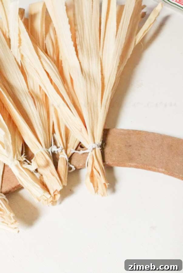 Floral wire being wrapped around the wide end of a corn husk for attaching to a wreath form