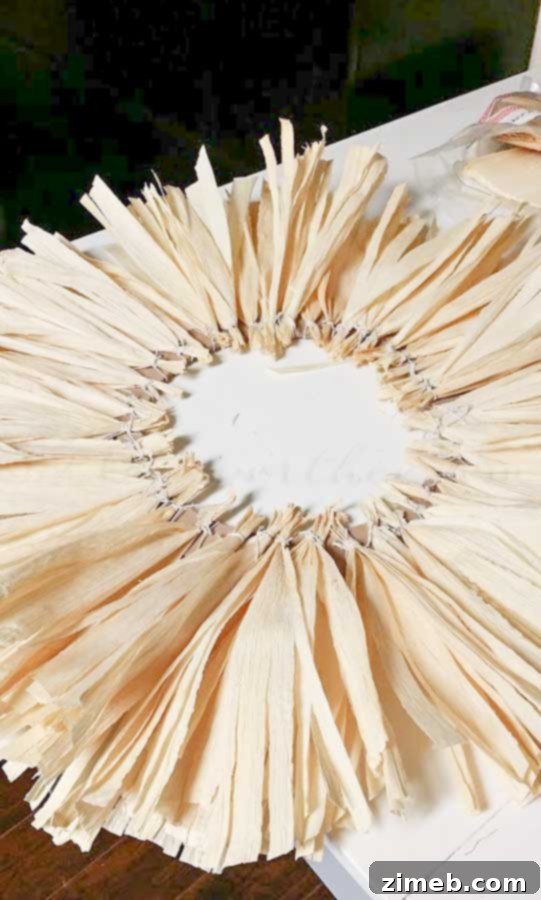 A wreath form progressively being covered with layered corn husks, creating a full texture
