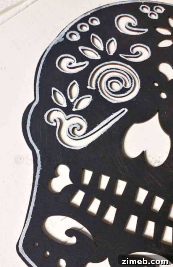 A black sugar skull cutout being decorated with a white paint marker, outlining features