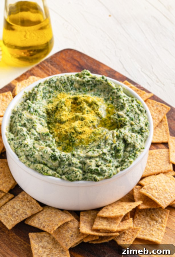 Irresistible Vegan Spinach Artichoke Dip 9 Game day dip: Vegan Spinach Artichoke Dip served on a rustic wooden board with assorted crackers and fresh vegetables.