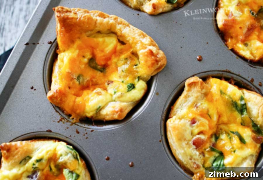 Close-up of freshly baked Bacon Cheddar & Spinach Quiche Cups in a muffin tin, showcasing the golden puff pastry and savory filling.