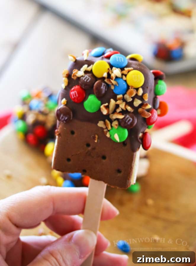 Irresistible Ice Cream Sandwich Pops 4 A collection of decorated Ice Cream Sandwich Pops, some with chocolate and sprinkles, others with nuts, on a parchment-lined baking sheet.