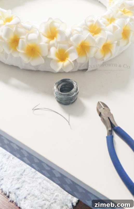 Tropical Plumeria Wreath 6 Hand applying vibrant foam plumeria flowers to a wreath form, demonstrating the step-by-step DIY process for a summer wreath.