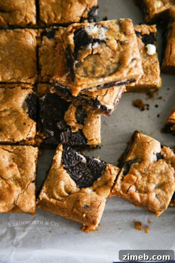 Oreo Peanut Butter Blondie Delights 4 A stack of golden brown Oreo Stuffed Peanut Butter Blondies on a white surface, with a bite taken from one, revealing the Oreo inside.