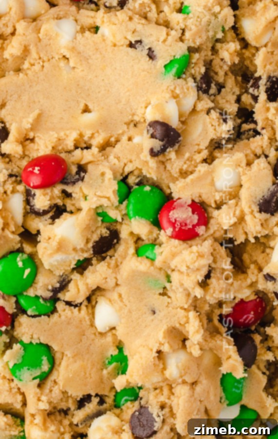 Close-up of vibrant red and green M&Ms mixed into chocolate chip cookie dough.