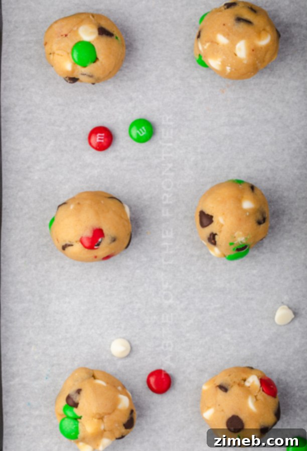 Unbaked cookie dough balls with red and green M&Ms, perfectly portioned on a baking sheet.