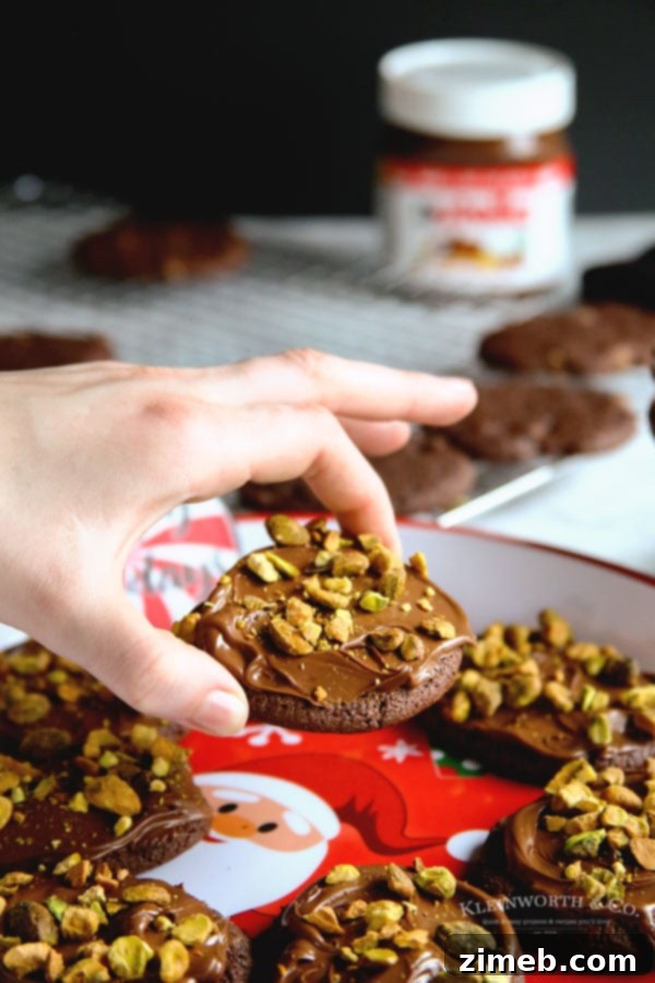 A stack of chocolate holiday cookies, each adorned with Nutella and pistachios.
