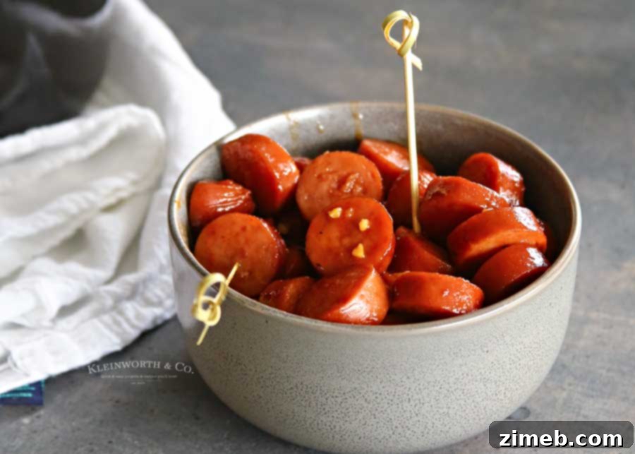 Sticky Sweet and Spicy Slow Cooker Sausage 5 A serving dish filled with Slow Cooker Sweet & Spicy Sausage, ready for guests to enjoy at a party.