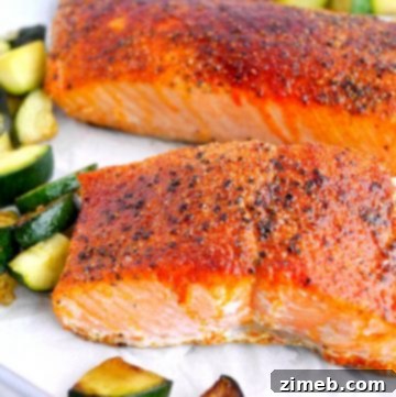 Close-up of perfectly cooked salmon fillets on a white plate with air fryer zucchini pieces scattered on the plate.