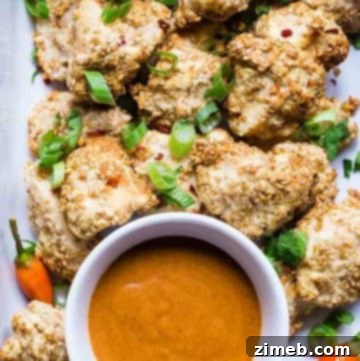 Overhead view of low-carb, keto-friendly baked chicken nuggets with a golden, crispy coating, arranged on a white plate, accompanied by a small bowl of dipping sauce,