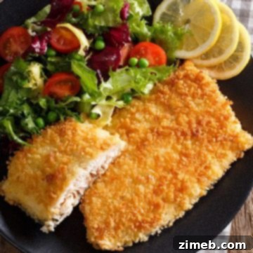 Overhead view of crispy air-fried fish filets, with a golden-brown breaded coating, served on a dark plate with lemon slices and a fresh side salad.