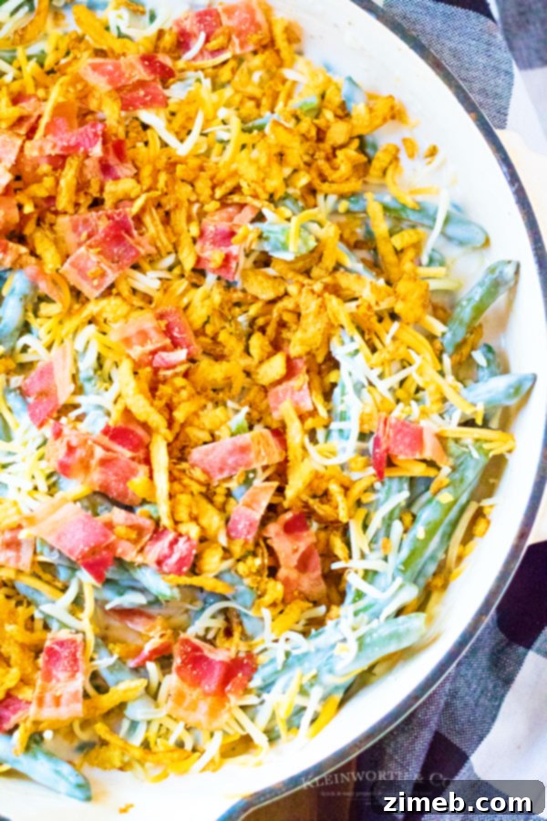 Ultimate Green Bean Bake 7 Green Bean Casserole ingredients before baking, topped with cheese, bacon, and fried onions.