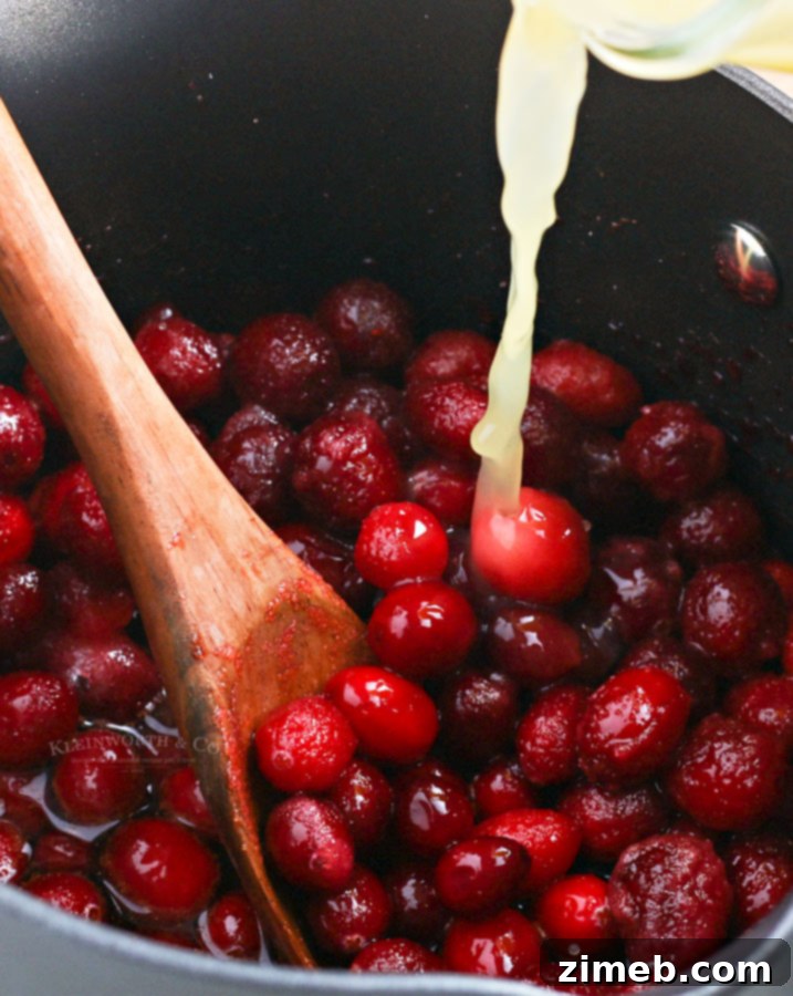 Effortless Cranberry Sauce 7 Orange juice and water being poured over the cranberry mixture in a saucepan, initiating the cooking process for the sauce.