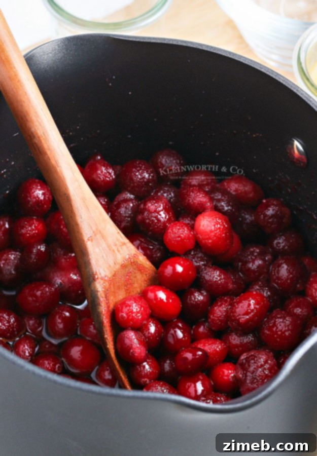 Effortless Cranberry Sauce 8 Cranberry mixture simmering in a saucepan, showing the berries beginning to soften and burst as the sugars dissolve.