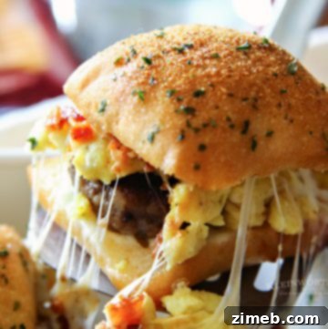 A close-up of breakfast sliders featuring layers of sausage, bacon, egg, and melted cheese sandwiched between golden brown slider buns, arranged neatly on a white platter.