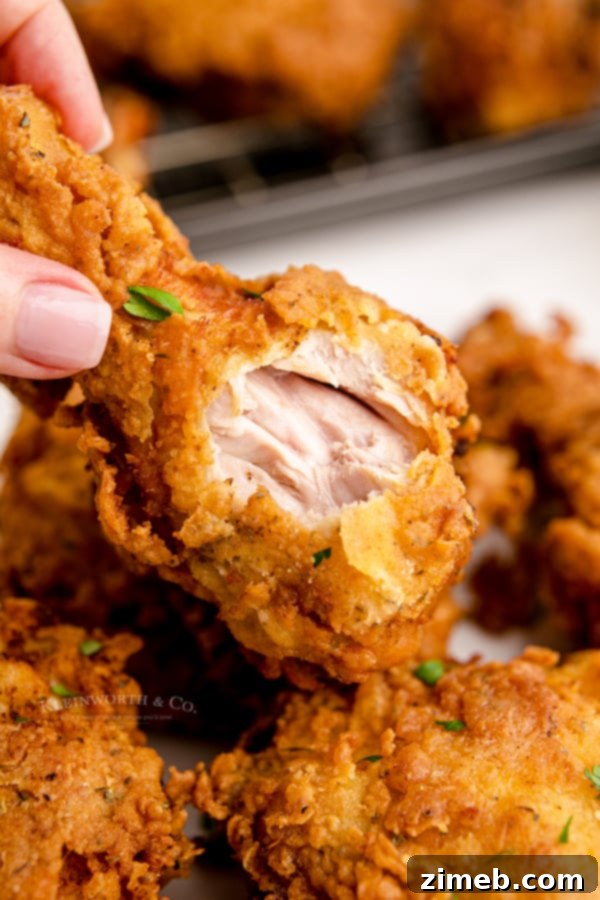 Bite of fried chicken, showing crispy skin and juicy meat