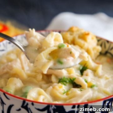 A bowl of comforting chicken pot pie noodle soup, filled with tender chicken, wide noodles, carrots, peas, and a creamy broth. The soup looks hearty and rich, capturing the essence of a classic chicken pot pie in a warming soup form. The colorful ingredients are beautifully mixed, creating an inviting and cozy meal.