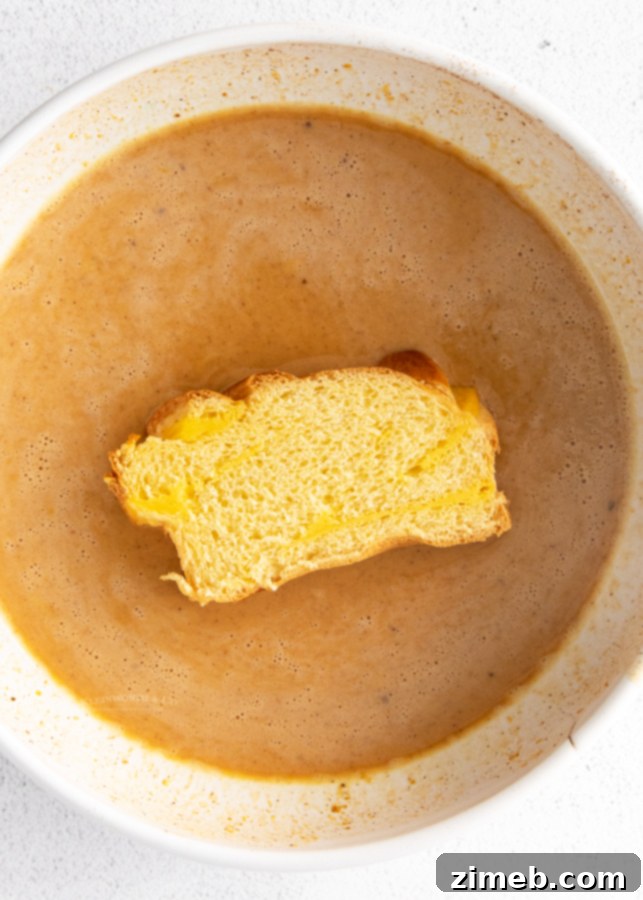 Hand dipping brioche bread into pumpkin French toast batter