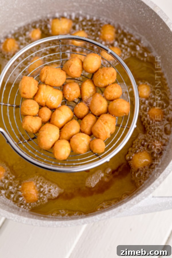 A slotted spoon lifting golden-fried Struffoli balls from hot oil