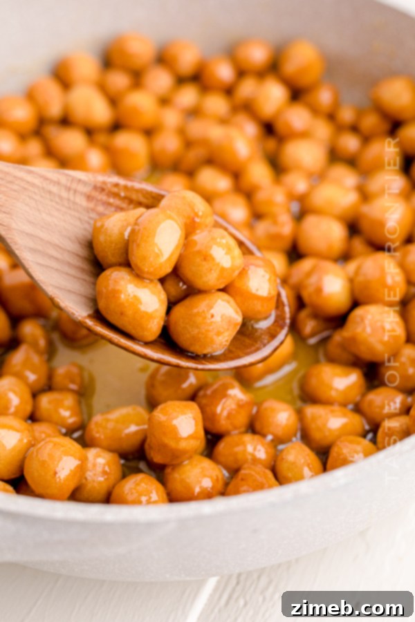 Struffoli being coated in a shimmering honey sauce within a large pot