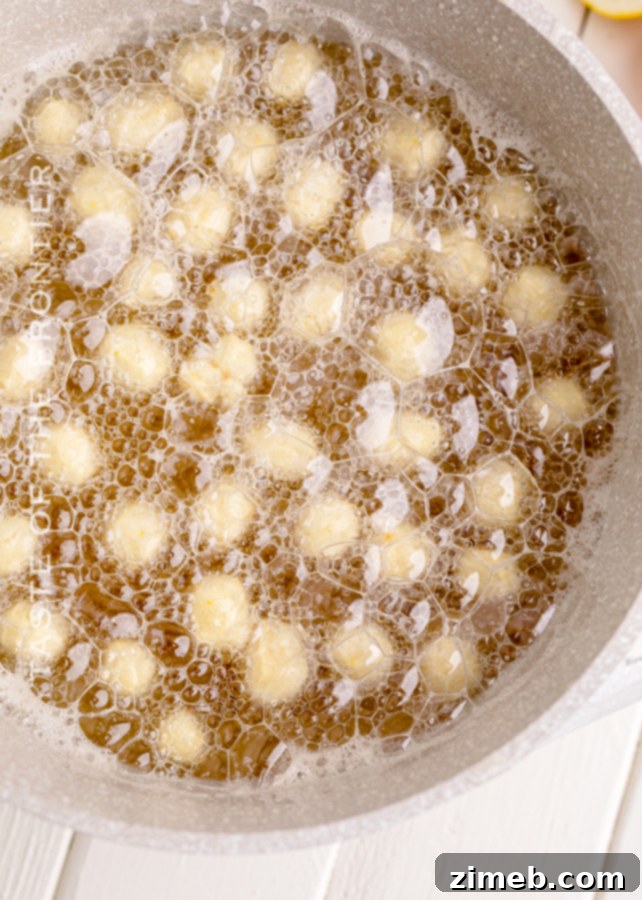 Struffoli dough balls being fried to a golden crisp in hot oil
