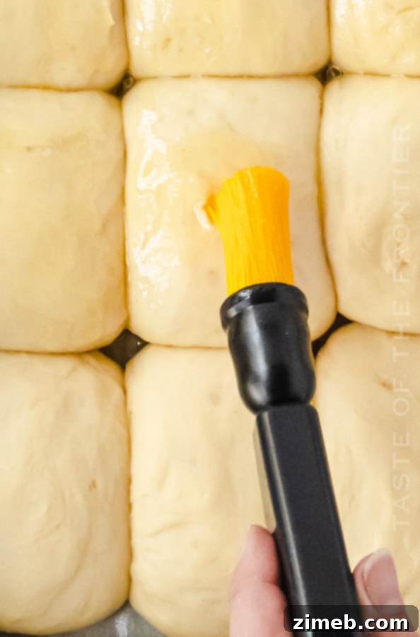 Brushing the golden brown rolls with melted butter for a soft finish