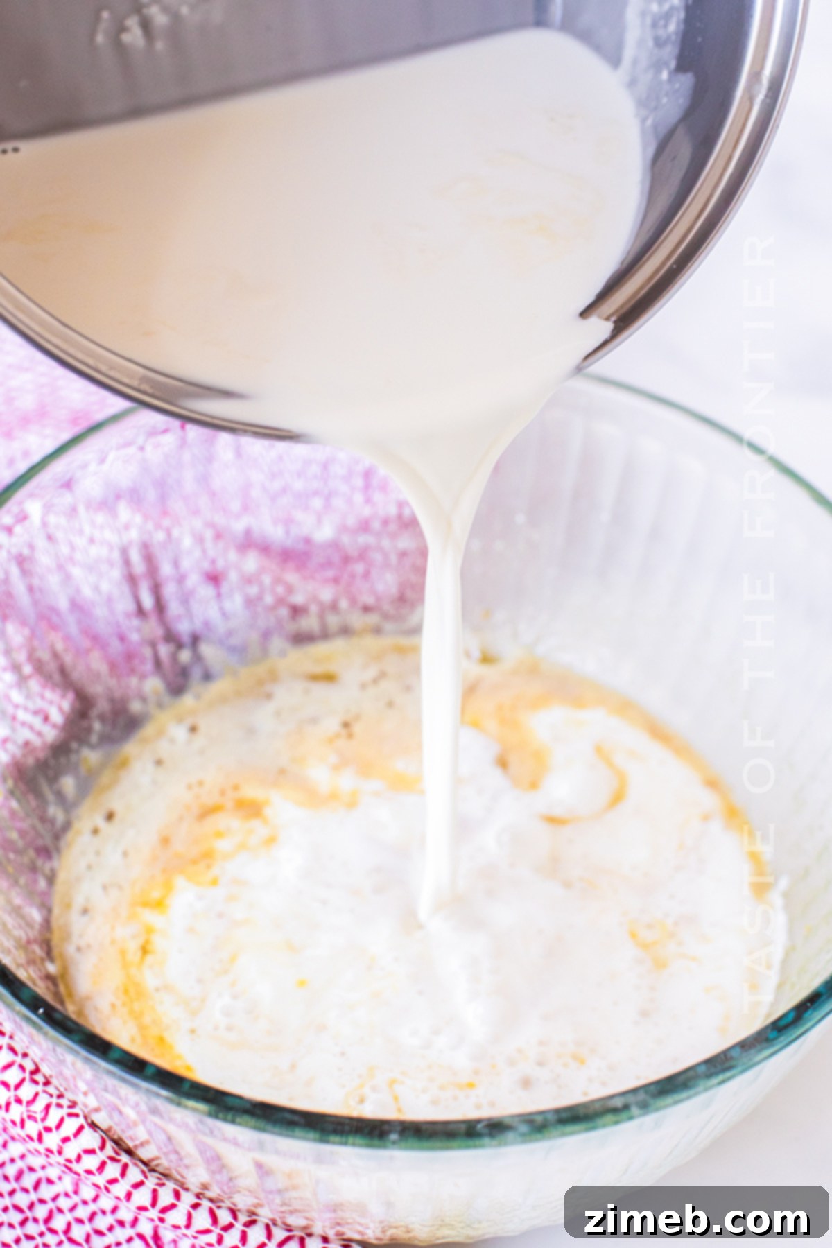 Pouring the creamy custard mixture over the bread and raspberries in the pan, preparing for a delightful breakfast bake.