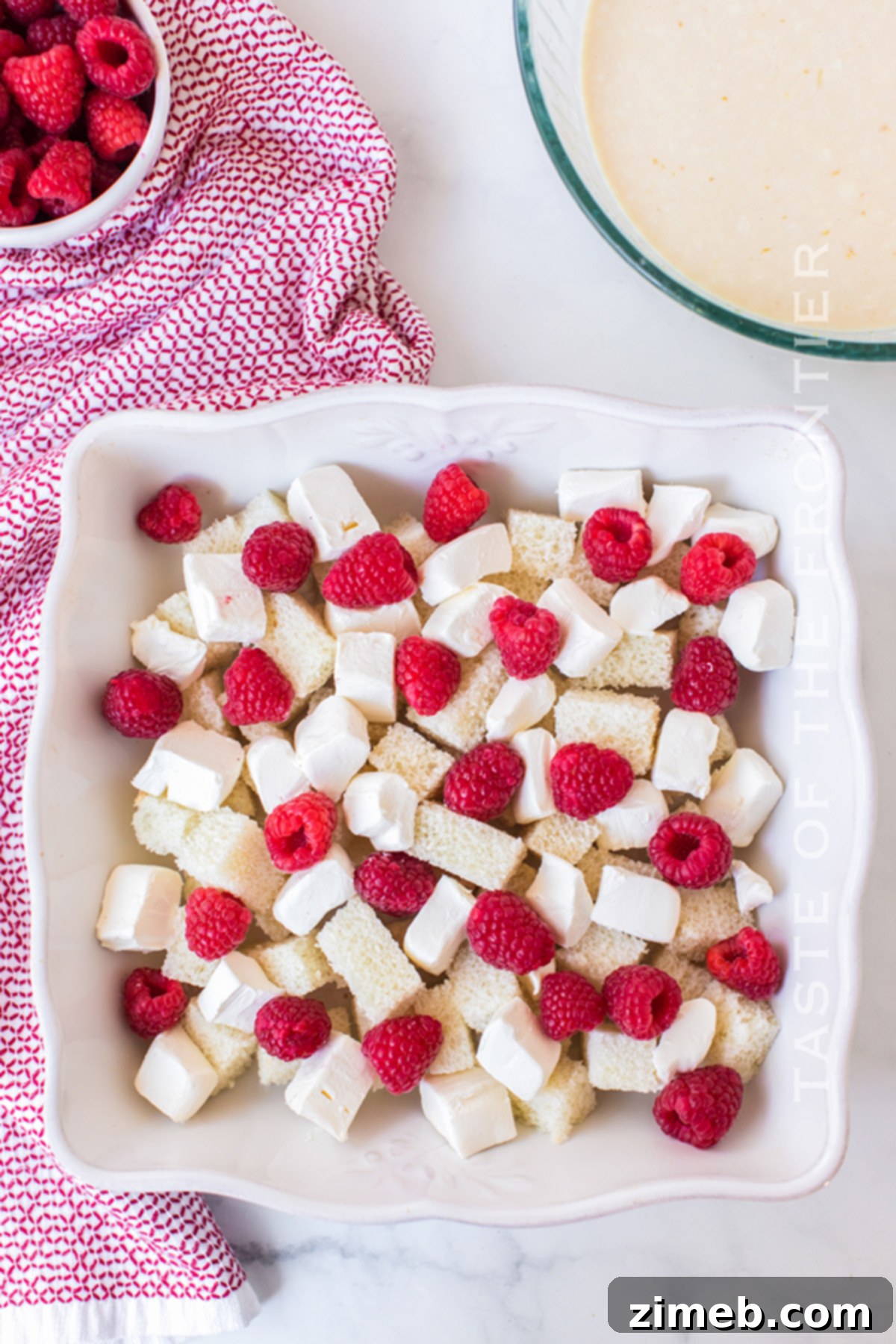 Bread, raspberries, and cream cheese arranged in the pan before adding the egg mixture, showcasing the casserole's foundational layers.