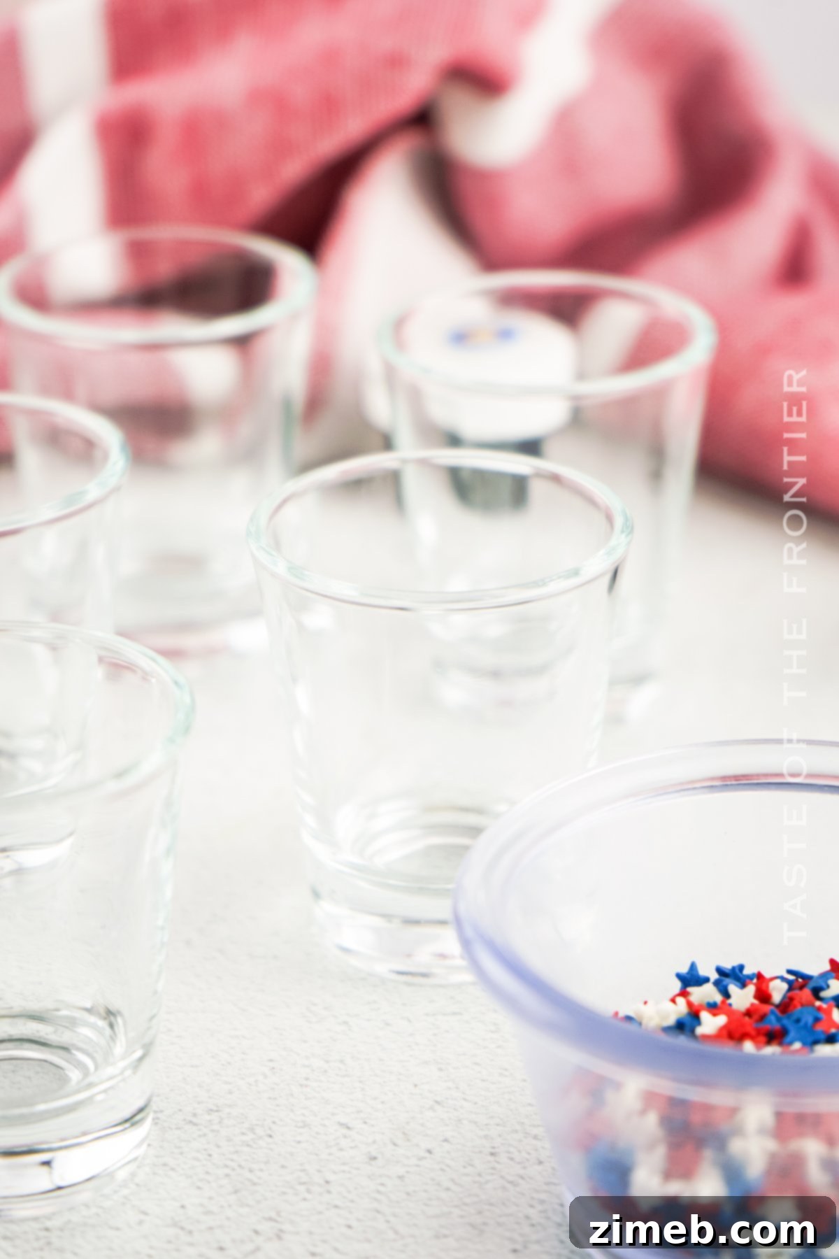 Boozy Pudding Delights 8 Shot glasses filled with Red, White, and Blue Pudding Shots, garnished with whipped cream and sprinkles.
