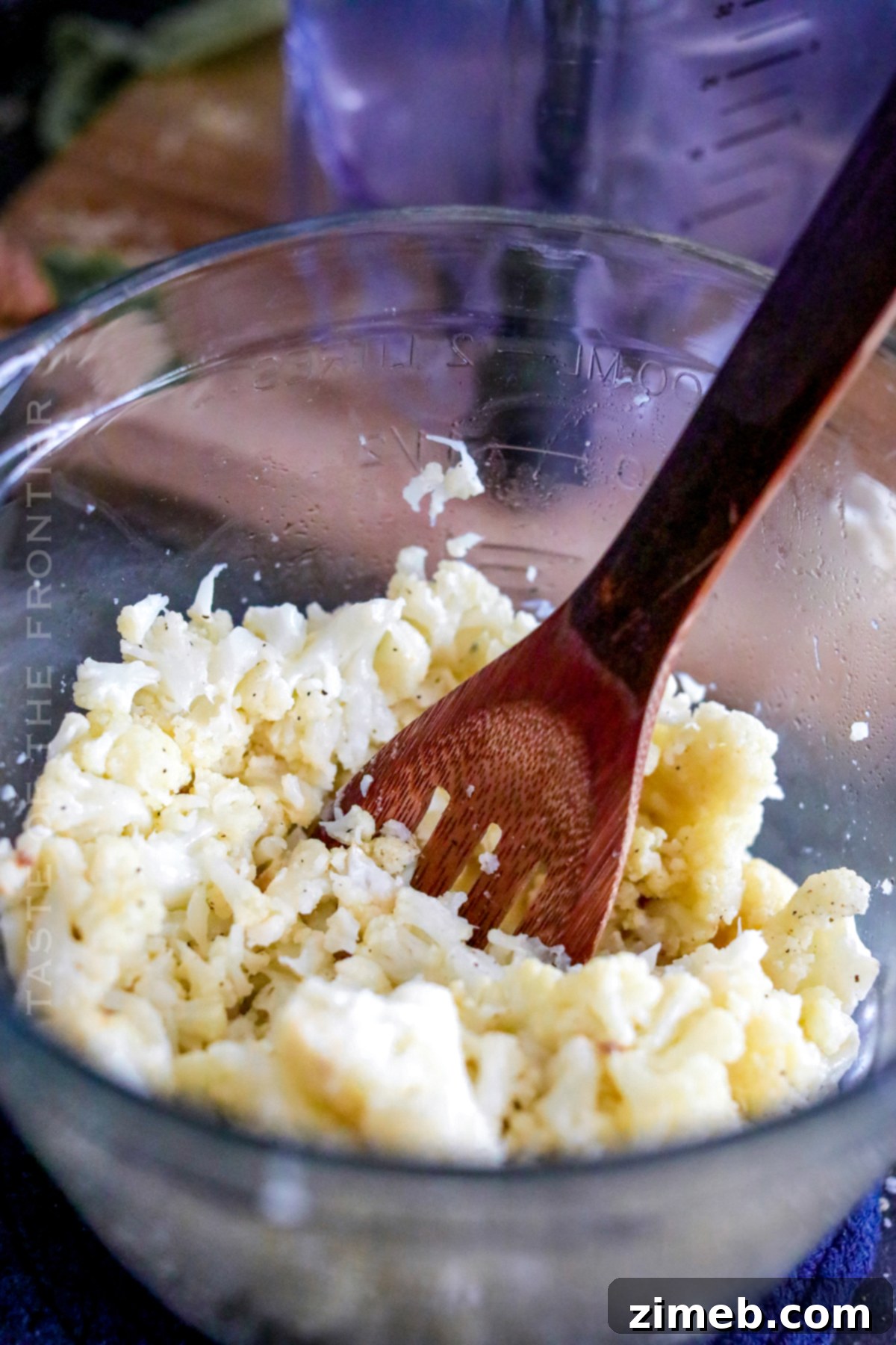 Mashing cauliflower with a tool in a bowl.