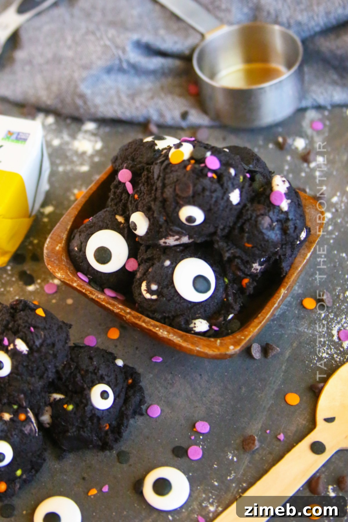 Edible Halloween Cookie Dough 3 Close-up of dark edible cookie dough in a bowl, featuring mini chocolate chips and candy eyeballs, a perfect Halloween treat.