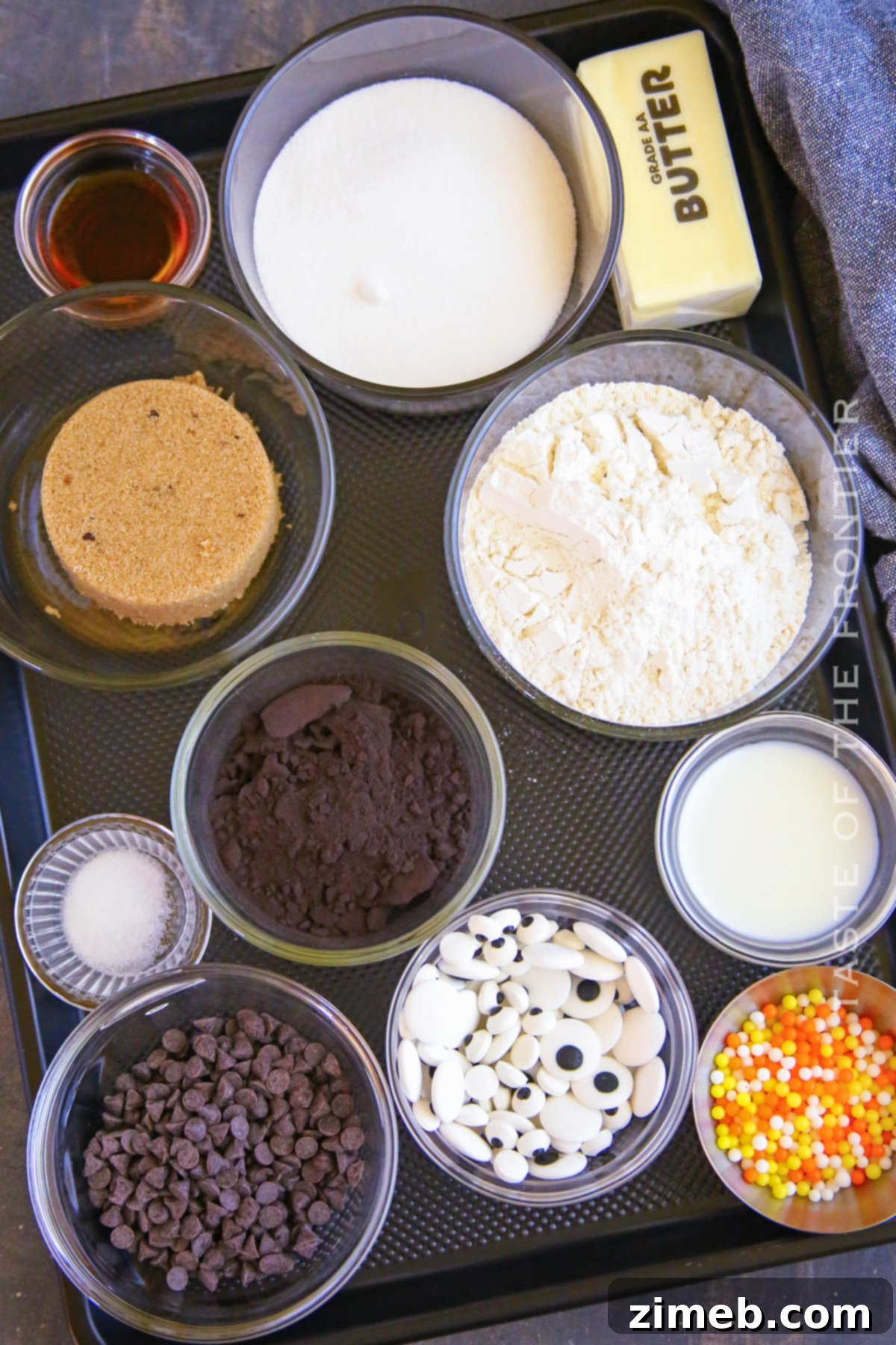 Edible Halloween Cookie Dough 4 Ingredients laid out for Halloween Cookie Dough: butter, sugars, black cocoa, milk, vanilla, flour, salt, candy eyeballs, chocolate chips, and sprinkles.