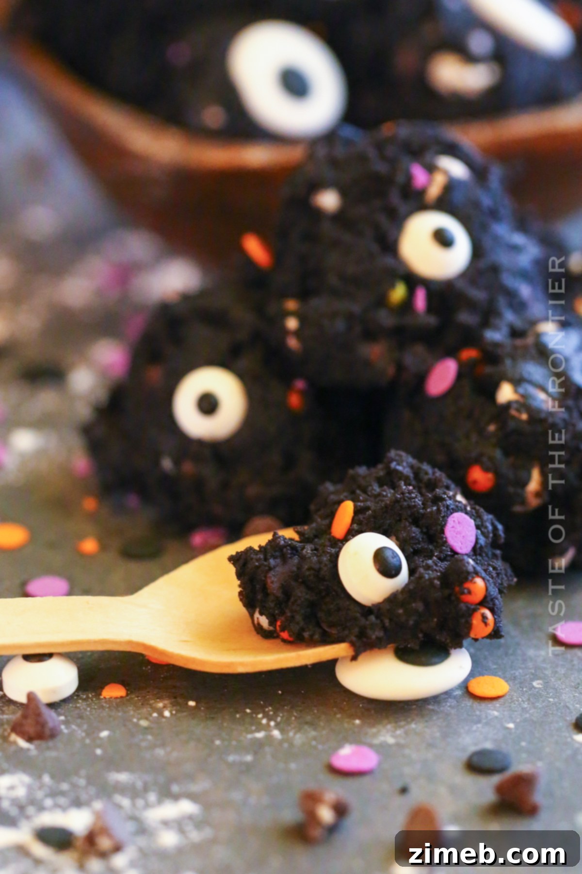 Edible Halloween Cookie Dough 6 Close-up of small, dark chocolate cookie dough balls decorated with candy eyeballs and sprinkles, arranged on a white plate.